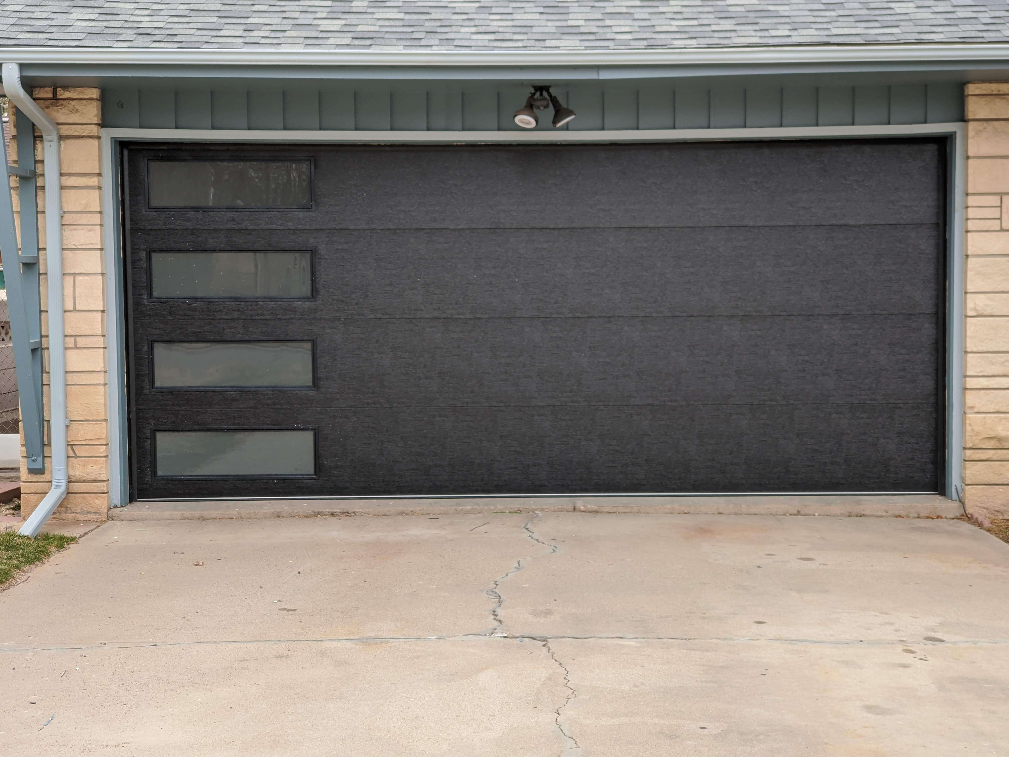 Modern black flush-panel garage door with vertical windows installed in Pueblo