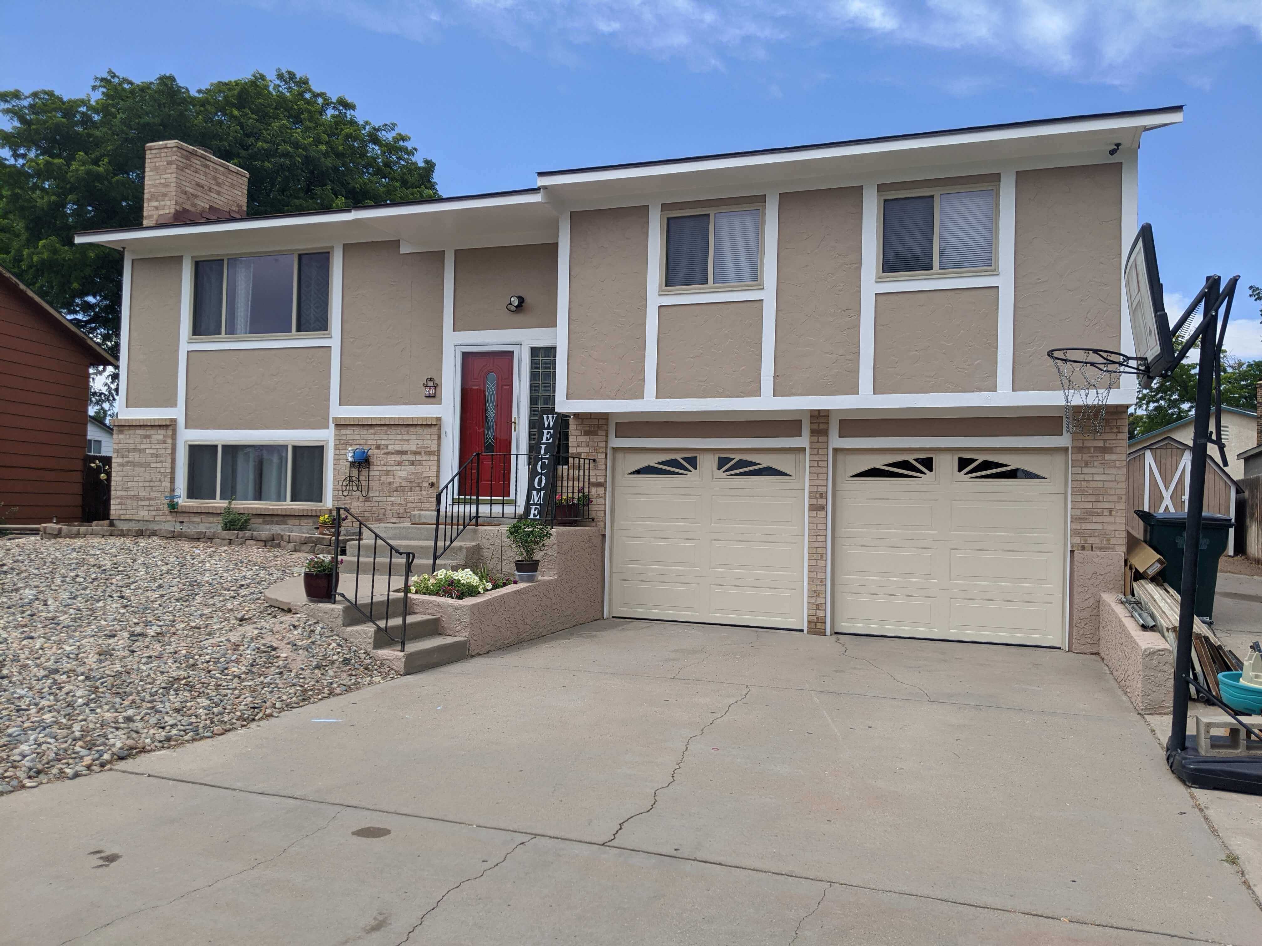 Two cream raised-panel garage doors with sunburst windows on a Pueblo split-level home
