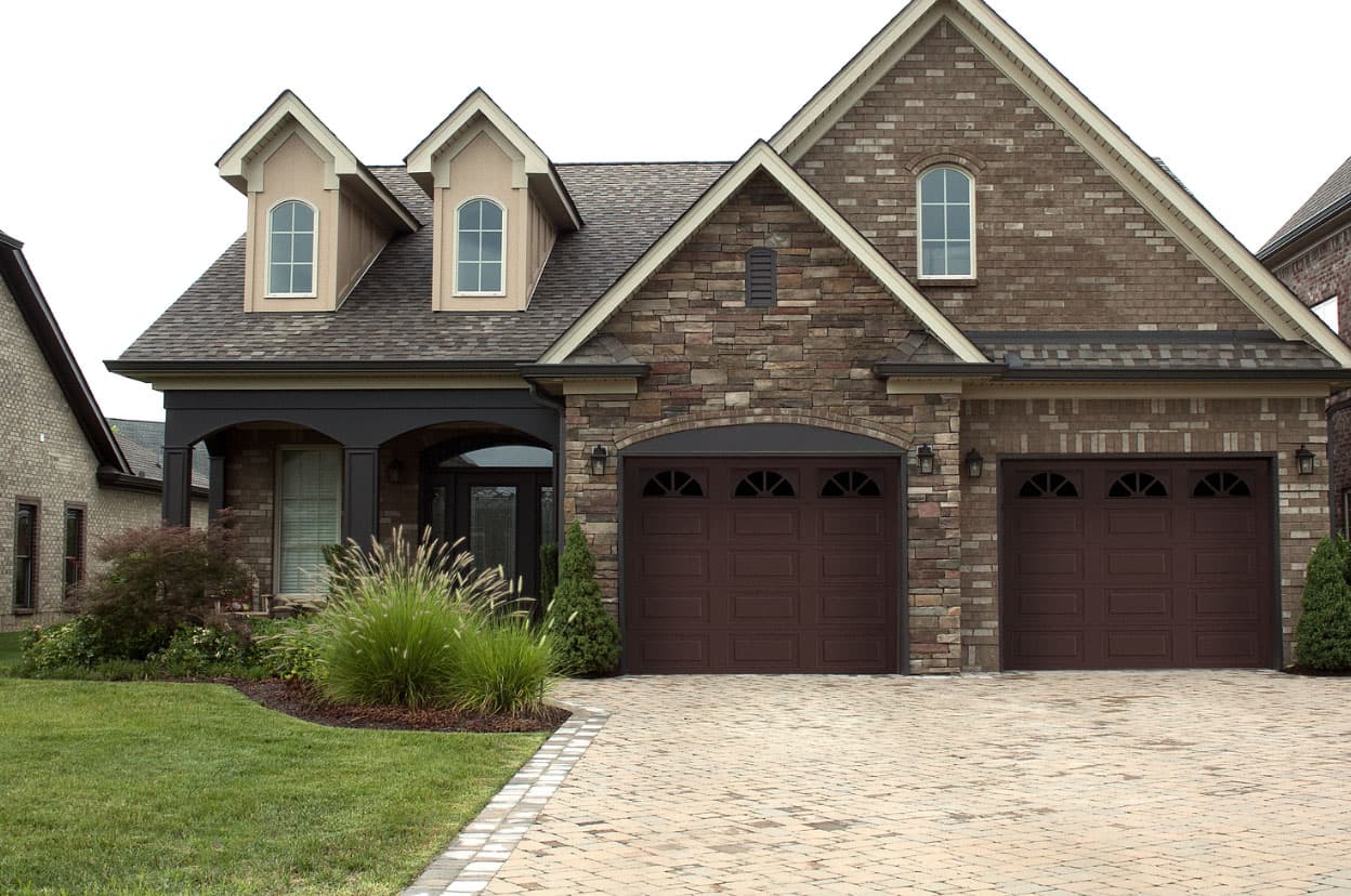 Raised-panel carriage garage doors with arched windows on a stone home